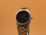 une montre noire et dorée posée sur un socle, sur fond jaune
