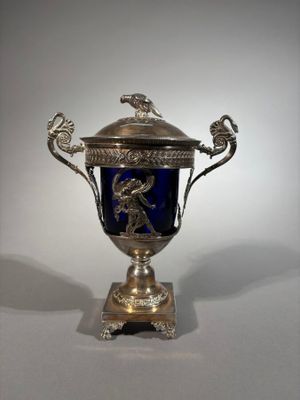a silver and blue vase on a stand with a bird on it