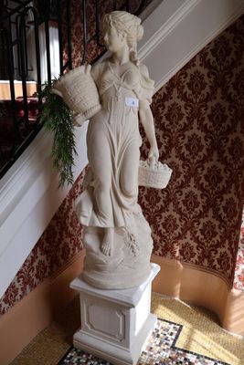 une statue représentant une femme tenant un panier de fleurs, posée sur un socle