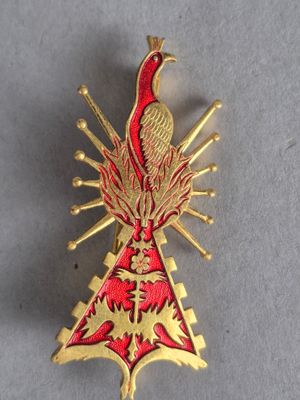 un gros plan sur une broche rouge et dorée ornée d'un oiseau