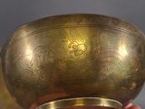 a person holding a brass bowl with a bird design on it