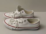 Des baskets Converse blanches avec des lacets rouges sont posées sur une surface blanche