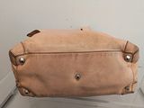 beige leather purse sitting on top of a glass shelf in front of a white wall