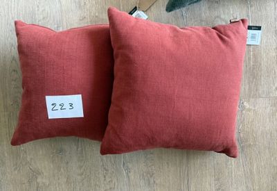 deux coussins rouges avec leurs étiquettes de prix, posés sur un parquet