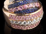 un gros plan d'une bague sertie de diamants roses, bleus et blancs, posée sur une surface noire