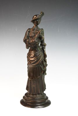 statue en bronze représentant une femme en robe et chapeau, avec un oiseau sur l'épaule