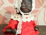 une poupée noire vêtue d'une robe rouge et d'un bonnet, assise sur une table