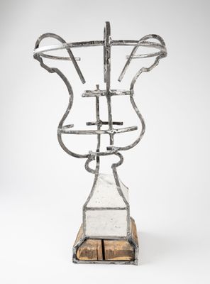 une photo d'une sculpture métallique représentant un vase posé sur un socle en bois
