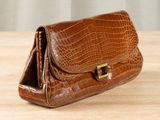 brown alligator skin purse on a wooden table with a curtain in the background