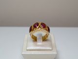 une photo d'une bague en or sertie de pierres rouges, posée sur un écrin blanc