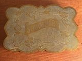 une plaque en or posée sur une table en bois, sur laquelle est inscrit un nom