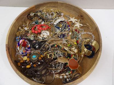 un bol en bois rempli de nombreux bijoux, posé sur une table