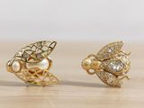 two pairs of gold and diamond bee earrings on a wooden surface
