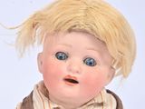 a baby doll with blonde hair and overalls sitting on a white surface