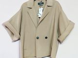La veste est de couleur beige clair et comporte un bouton noir sur le devant.