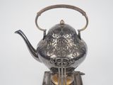 a silver tea pot with a handle on a stand