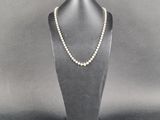 un collier de perles blanches sur un mannequin posé sur un socle noir
