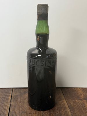 une vieille bouteille noire avec une étiquette verte posée sur une table en bois