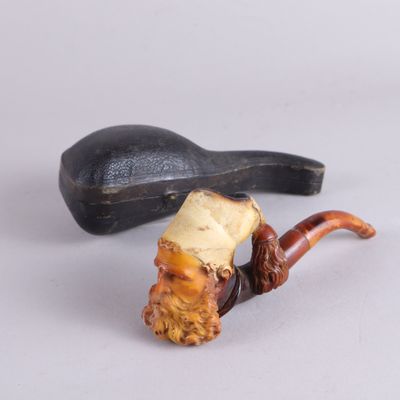 une pipe sur laquelle est représenté un visage d'homme, à côté d'un porte-pipe