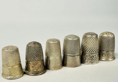 six antique thimbles lined up in a row on a white surface