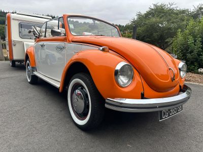 une Coccinelle Volkswagen orange et blanche garée sur un parking