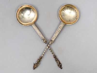paire de cuillères anciennes en argent avec des manches, posées sur une surface blanche