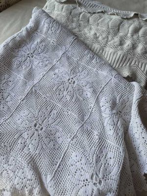 un pull blanc en maille posé sur un lit, à côté d'un oreiller