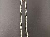a white pearl necklace with a gold clasp on a black background