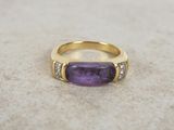 a gold ring with a purple stone and two diamonds