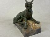 statue of a dog sitting on a piece of wood on a white surface