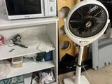 un ventilateur posé sur un support à côté d'un micro-ondes