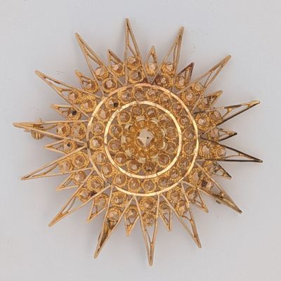 une broche en or ornée de pointes, posée sur un fond blanc