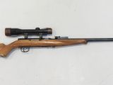 un fusil posé sur une surface blanche, équipé d'une lunette de visée