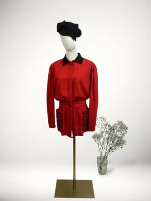 mannequin dressed in a red coat and black hat with a vase of flowers in front of it