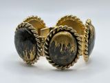 a close up of a gold and black bracelet on a white surface
