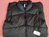 un gilet matelassé noir posé sur un lit recouvert d'une couverture rose