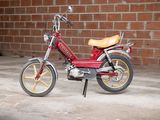 a small red motorcycle parked in front of a brick wall