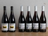 six bottles of wine are lined up on a wooden table