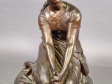 bronze statue of a woman sitting on a rock with her hands on her knees