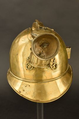 casque en laiton posé sur un socle noir, devant un fond noir