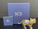 une figurine en verre représentant un lion, posée sur une table à côté d'une boîte bleue