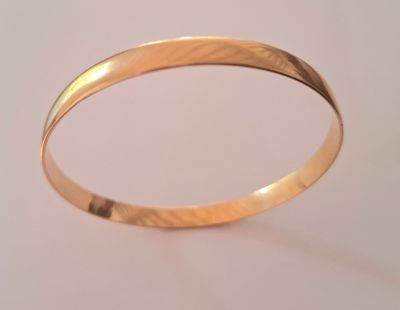gros plan d'un bracelet en or sur une surface blanche