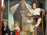 deux poupées dans une vitrine, avec un bateau en arrière-plan