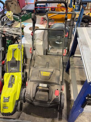 Plusieurs tondeuses à gazon sont alignées dans un garage où se trouvent également des outils.