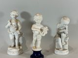 three figurines of children sitting on pedestals on a white surface