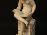 a statue of a boy sitting on a rock reading a book