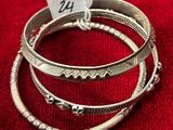 trois bracelets rigides en argent avec une étiquette, posés sur un tissu rouge