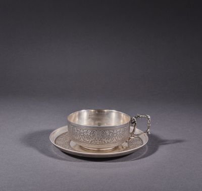 a silver cup and saucer on a saucer on a gray surface