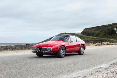 a red car driving down the road by the ocean
