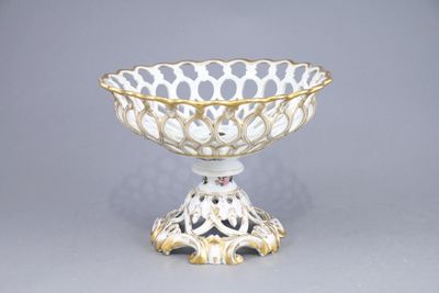 a white and gold bowl on a stand on a gray surface